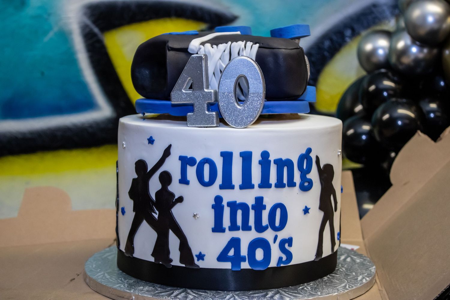 A 40th birthday cake decorated with silhouettes and 'rolling into 40s' text, topped with a roller skate.