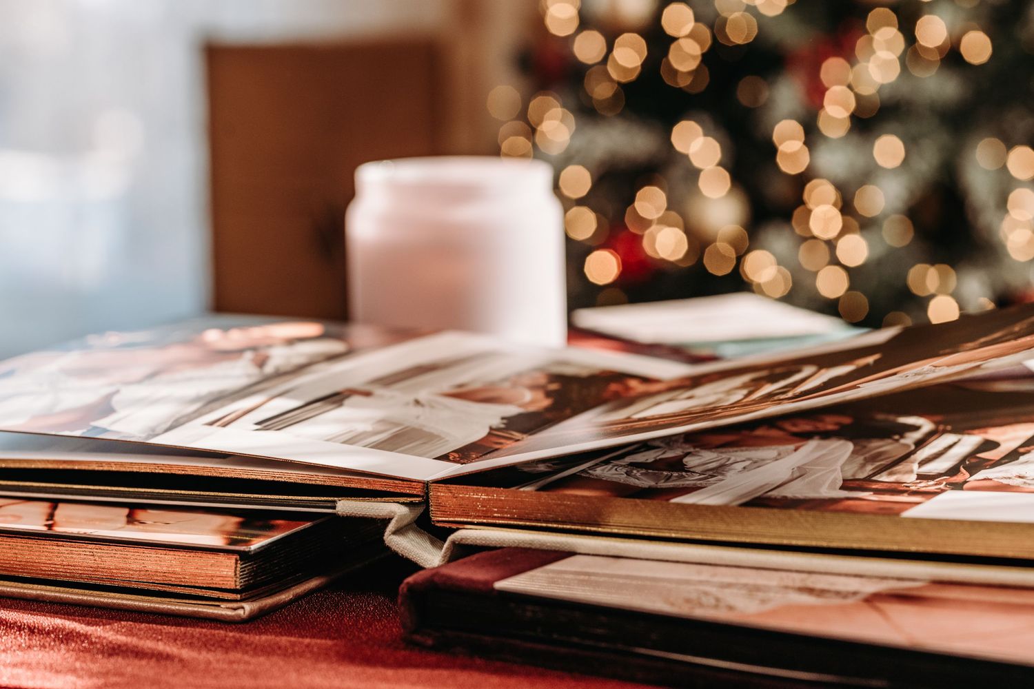 A collection of old photo albums and scrapbooks displayed on a wooden table with warm bokeh lights in the background.