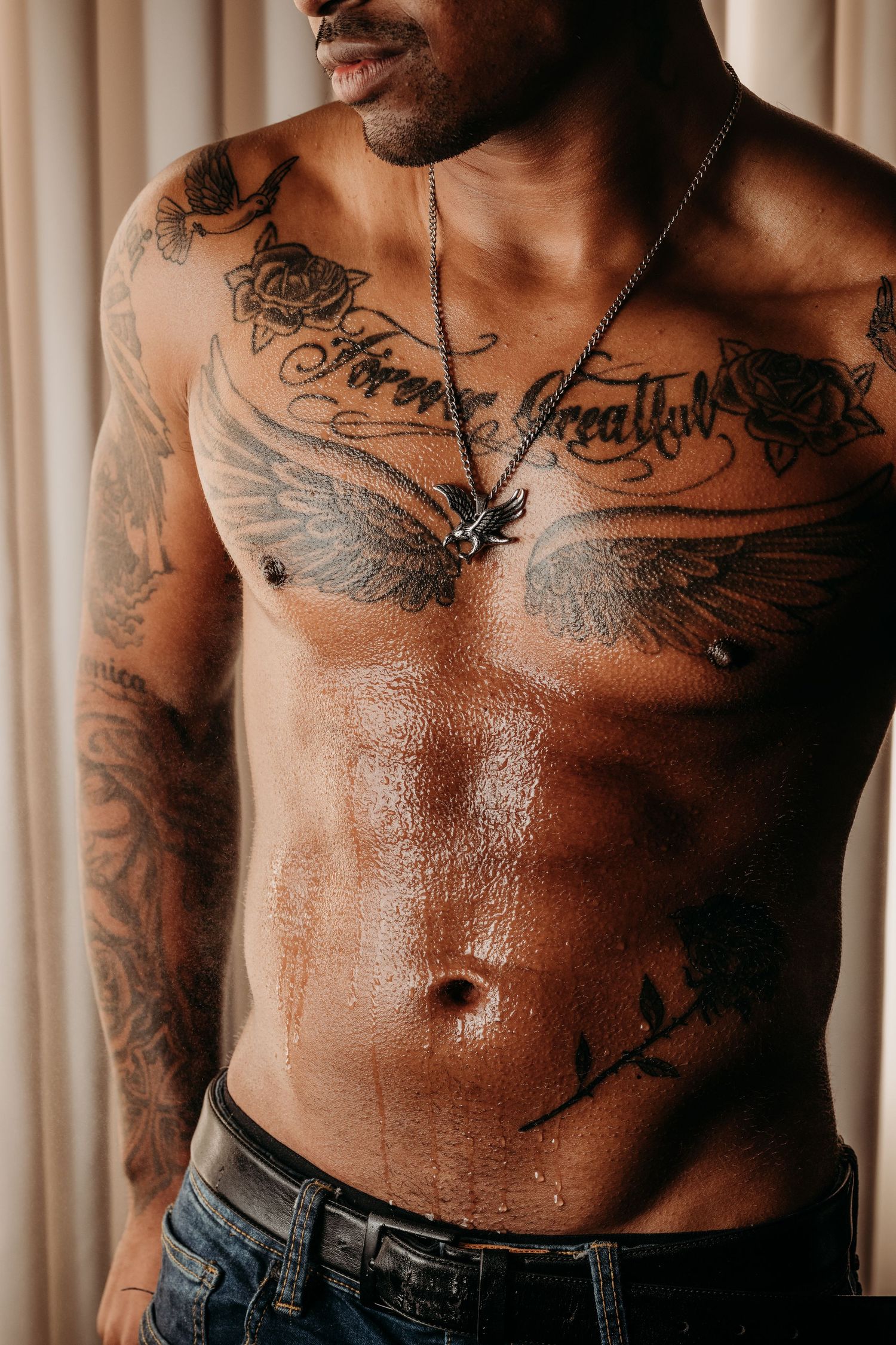 Close up of shirtless person with multiple tattoos showing their torso and chest against a curtained background. Boudoir Studio Rental Space