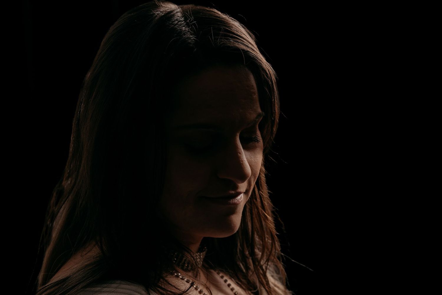 Young woman with long dark hair smiling softly, dramatically lit against a dark background.
