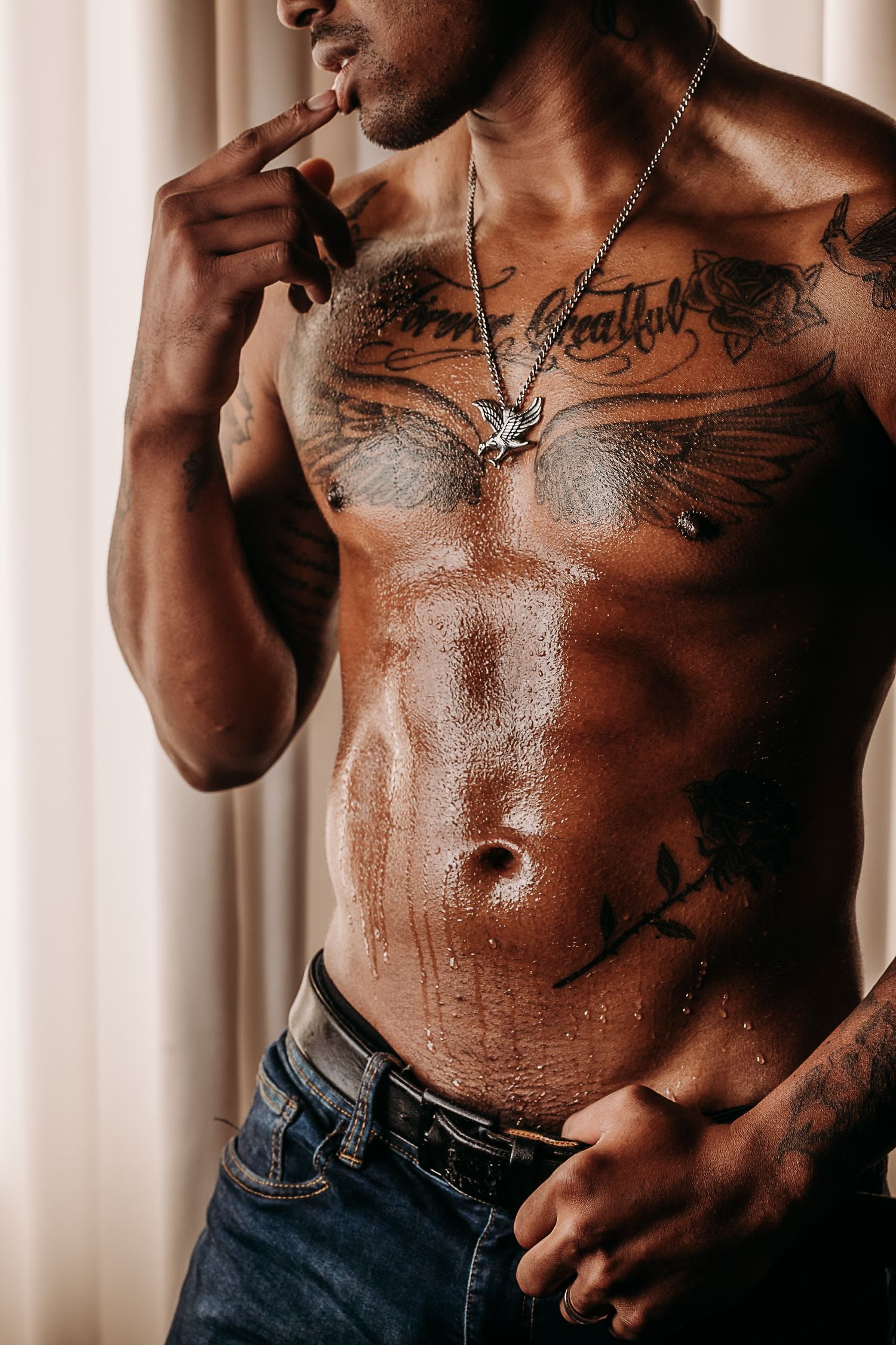 Shirtless torso with wing tattoo and necklace against white curtain background. Boudoir Photography Studio, Grand Rapids MI