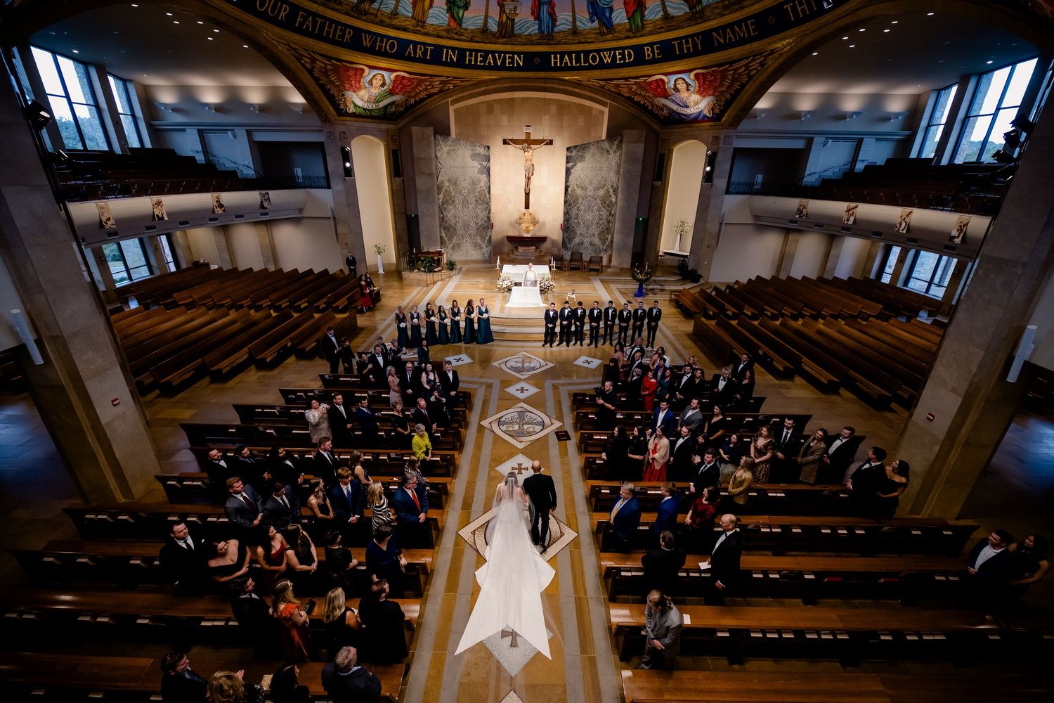 Aerial view of a wedding ceremony in an elegant church with wooden pews, floral aisle, and ornate altar.