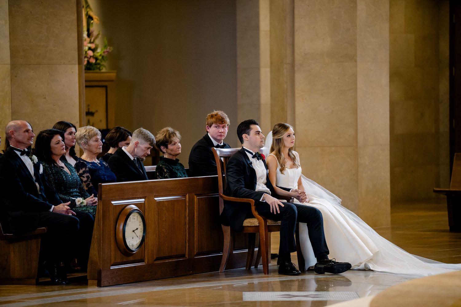 Bride and groom seated at church altar during wedding ceremony with guests in pews.