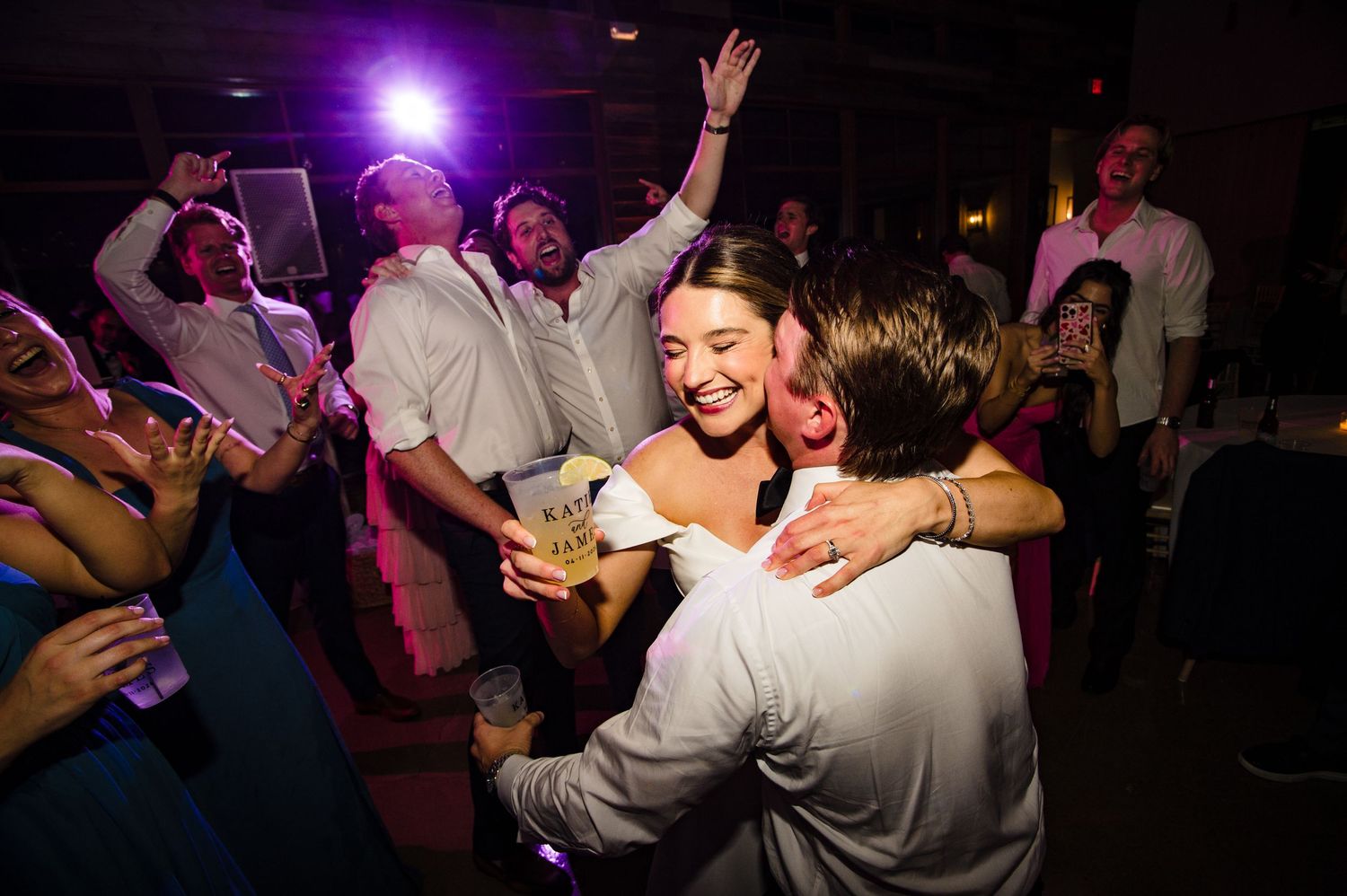 Bride hugging guest on wedding reception dance floor surrounded by celebrating friends under purple lights at Stonehouse Villas in Driftwood