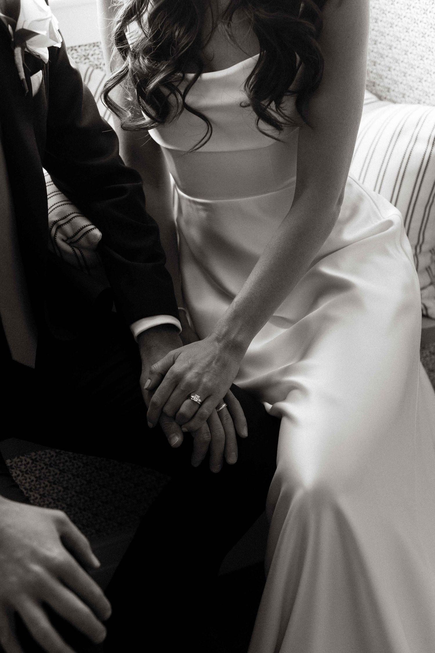 Black and white photo of bride and groom holding hands, showcasing elegant diamond engagement ring and wedding dress.