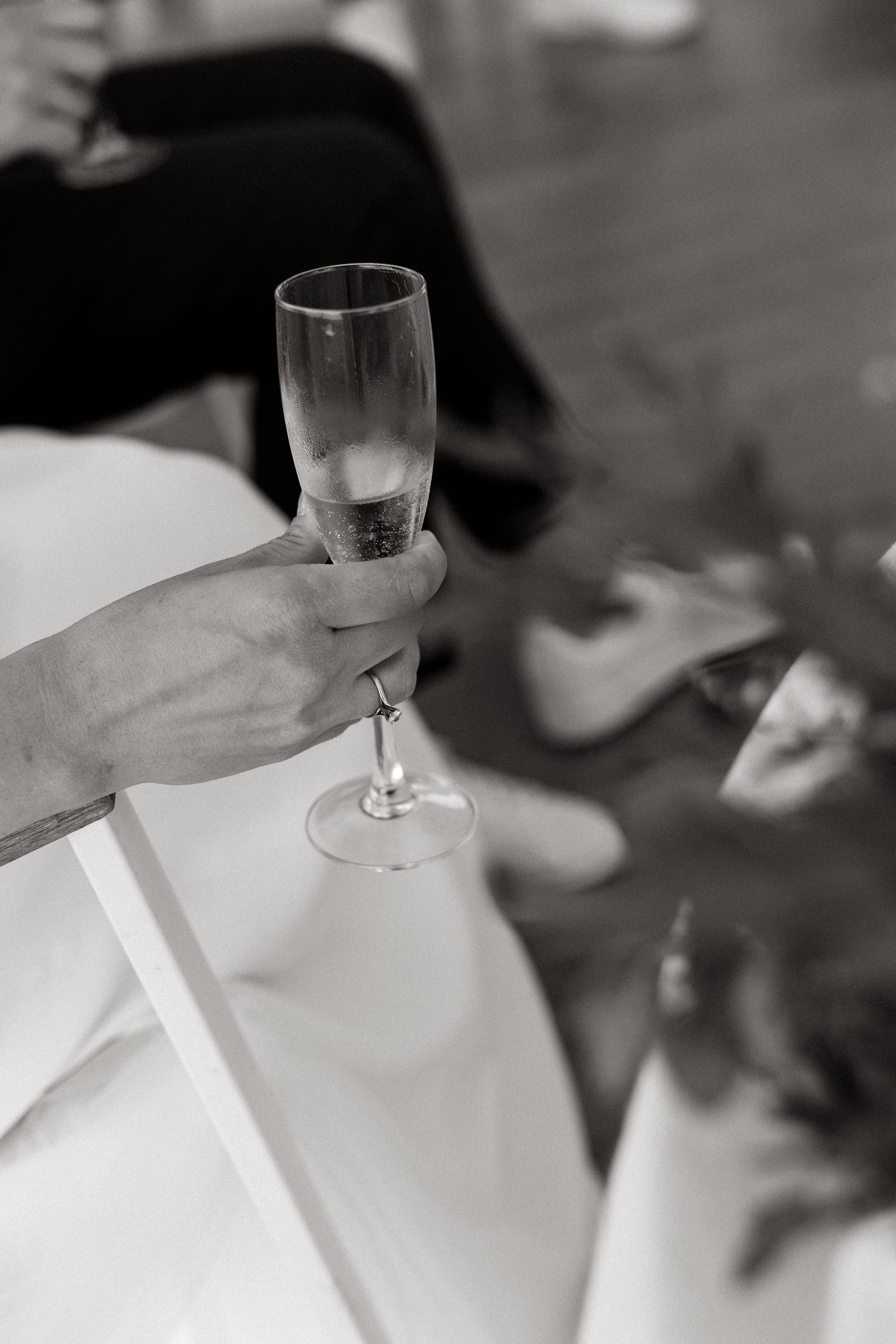 A hand holds an elegant champagne flute against a black and white background in an artistic celebration shot.