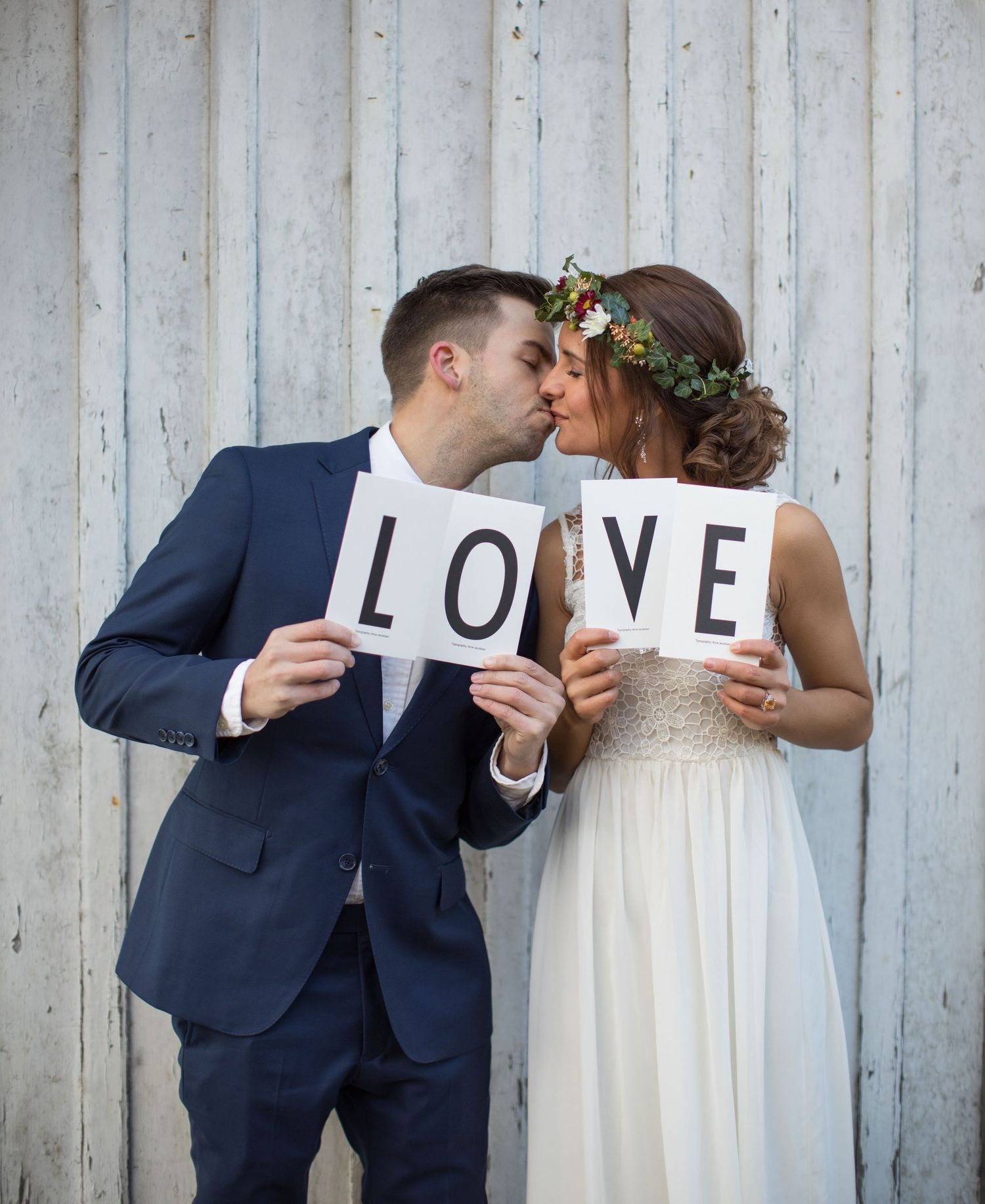 bröllopspar håller skylt med texten love bröllopsfotograftyresö bröllopityresö sensommarbröllop brud med blomsterkrans på huvet