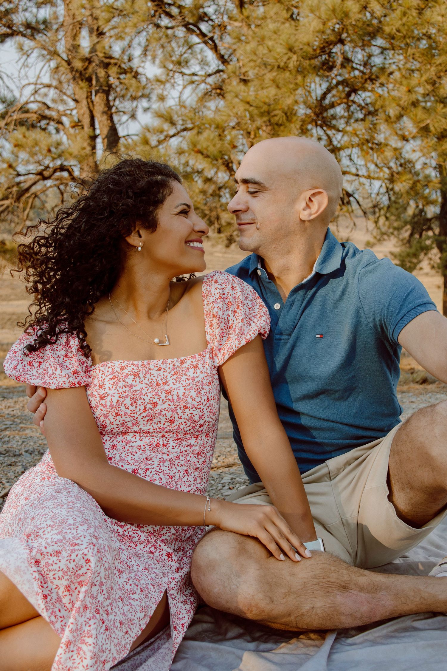 A couple sitting outdoors sharing a romantic moment together during autumn, with golden trees in the background.