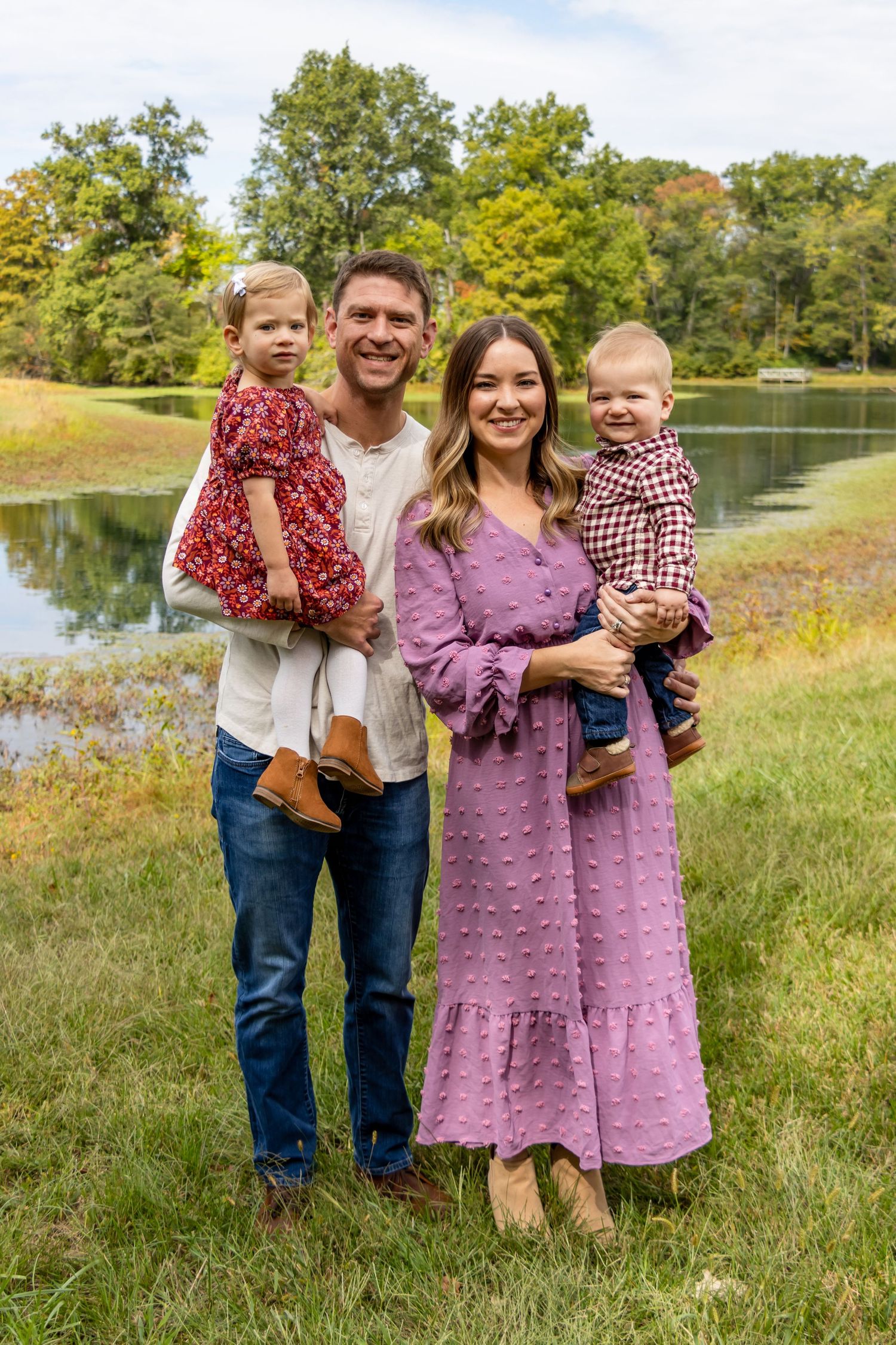 A family stands together on grass near a pond on an autumn day wearing coordinated red and purple outfits.