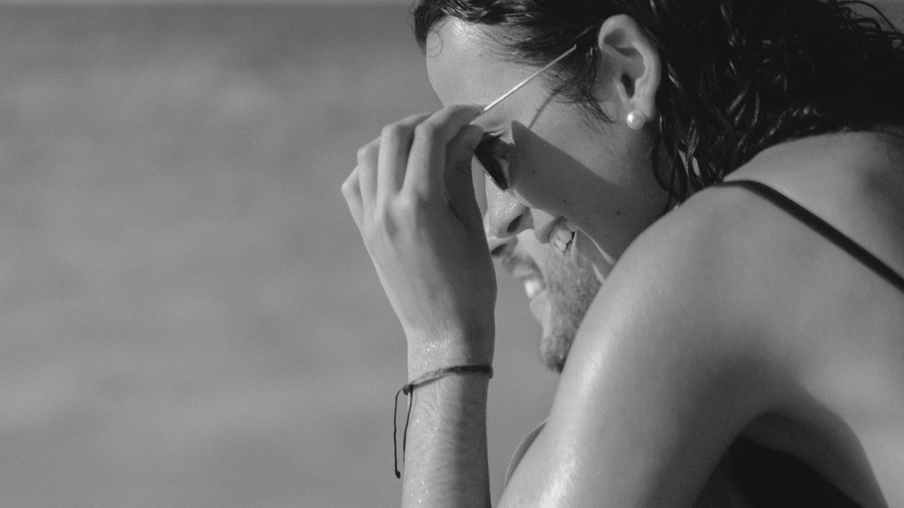 Black and white close-up of person wiping forehead in sunlight on warm day.