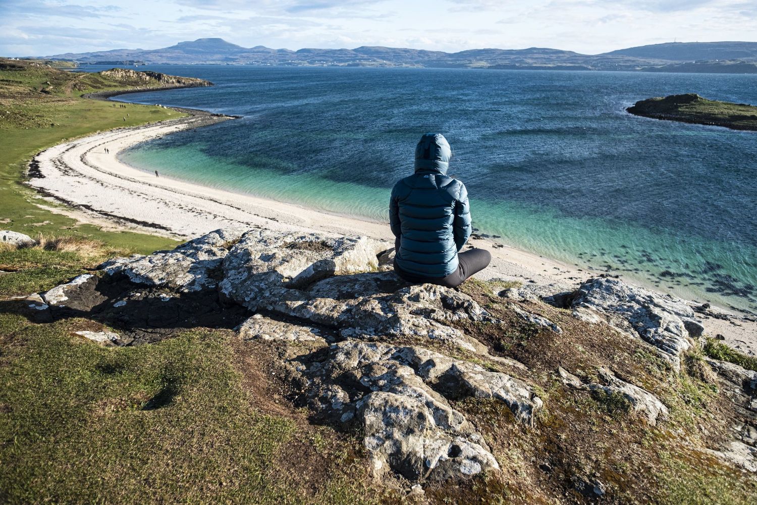 Une personne de dos contemple une plage de sable blanc et une eau turquoise depuis une falaise par Jérémie Botte.