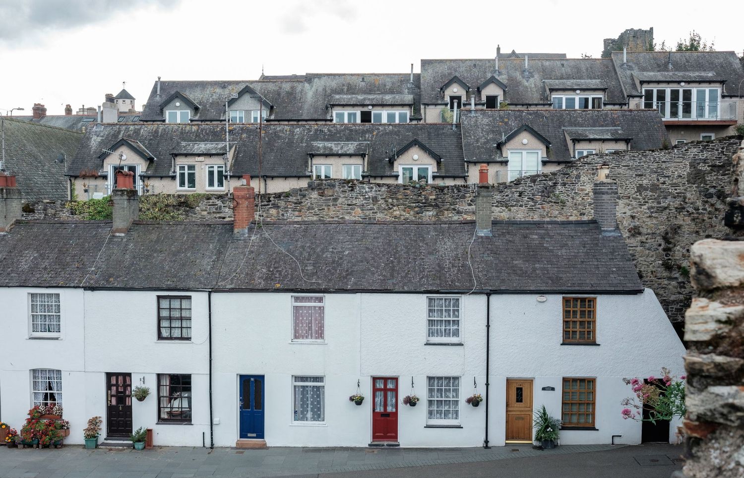 Alignement de petites maisons blanches aux portes colorées sur fond de village en pierre par Jérémie Botte.