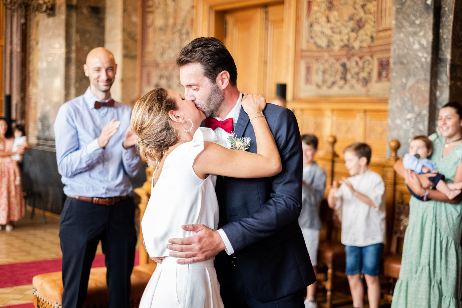 Un couple de mariés échange un baiser passionné à la maison communale sous les applaudissements des invités, par Jérémie Botte.