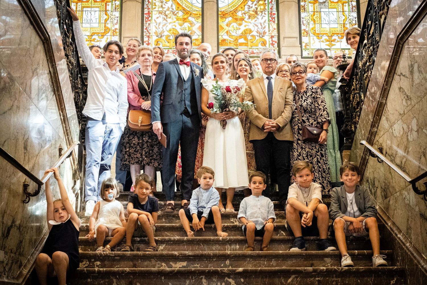 Photo de groupe réunissant les mariés, les invités et plusieurs enfants sur les marches d'un grand escalier, par Jérémie Botte.