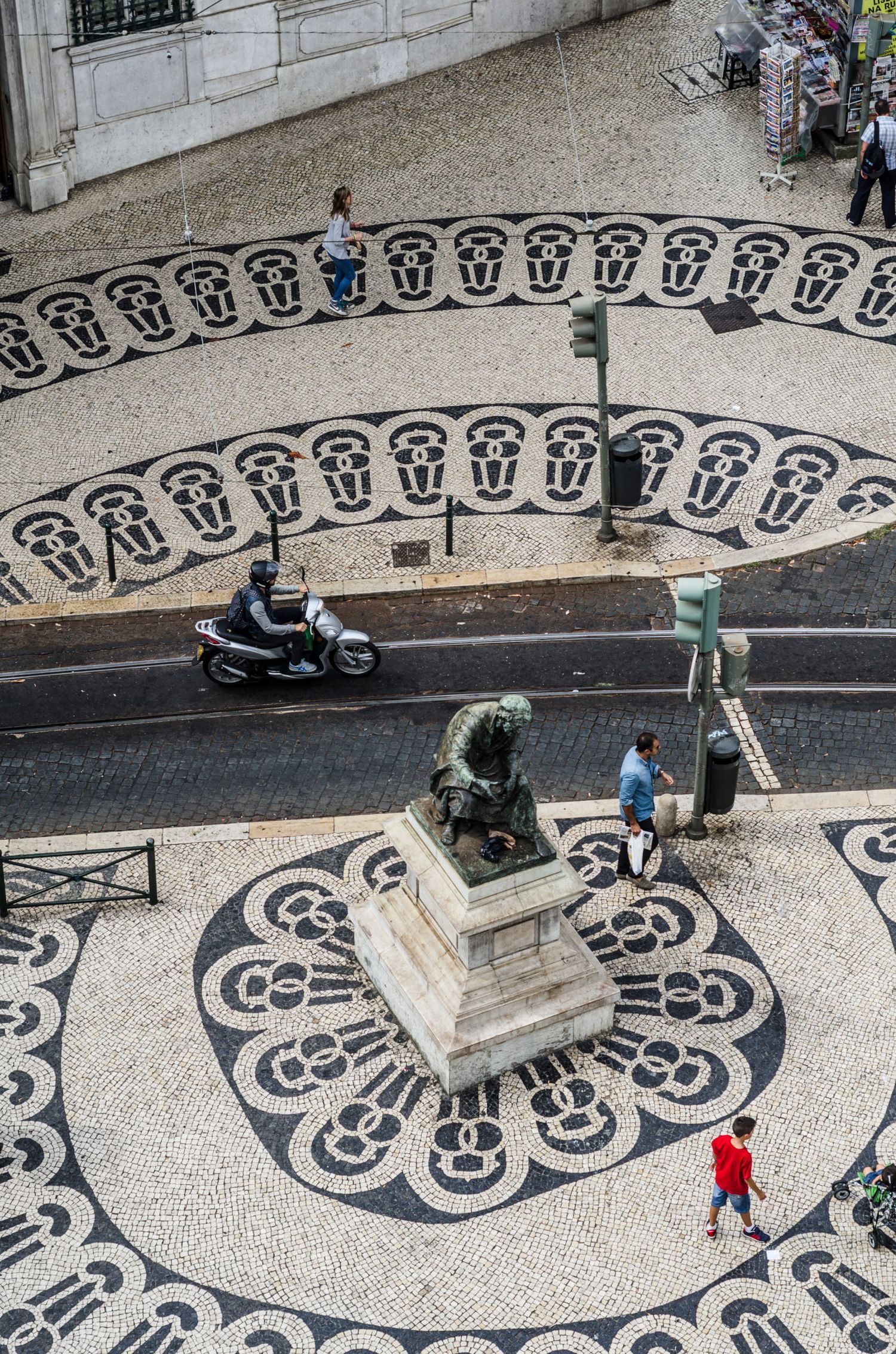 Une vue plongeante sur une place pavée aux motifs graphiques en noir et blanc avec une statue centrale au Portugal, par Jérémie Botte.