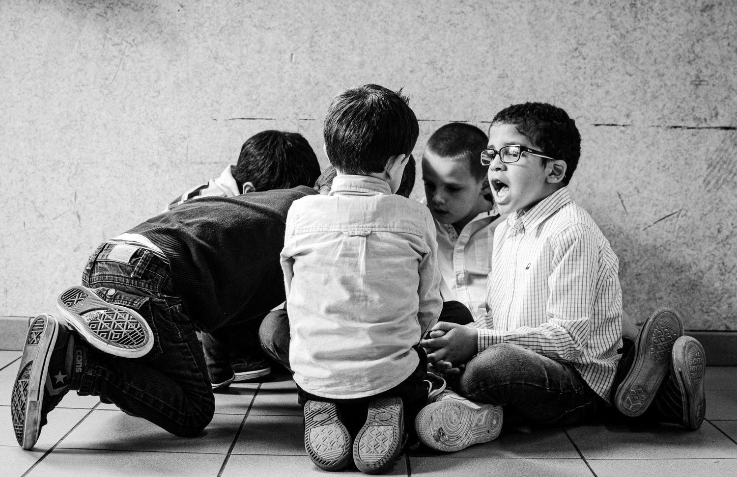 Photo en noir et blanc de plusieurs jeunes garçons assis en cercle par terre contre un mur par Jérémie Botte.