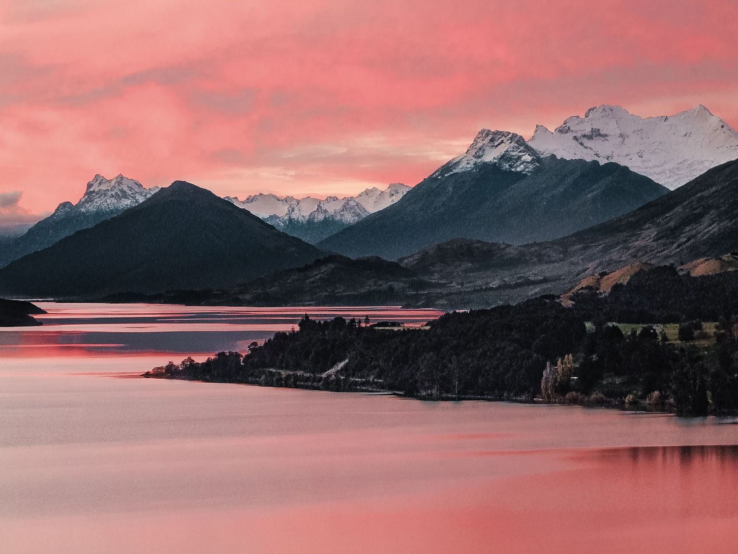 Chaîne de montagnes enneigées se reflétant dans un lac teinté par un coucher du soleil rose en Nouvelle-Zélande, par Jérémie Botte.