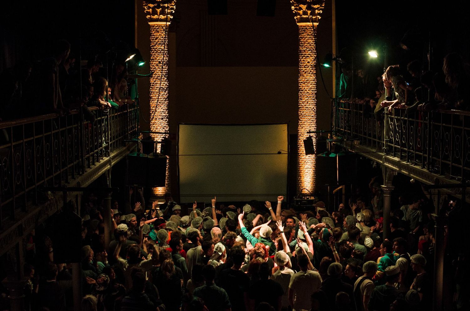 Une foule immense lève les mains lors d'un concert en intérieur devant un écran géant par Jérémie Botte.