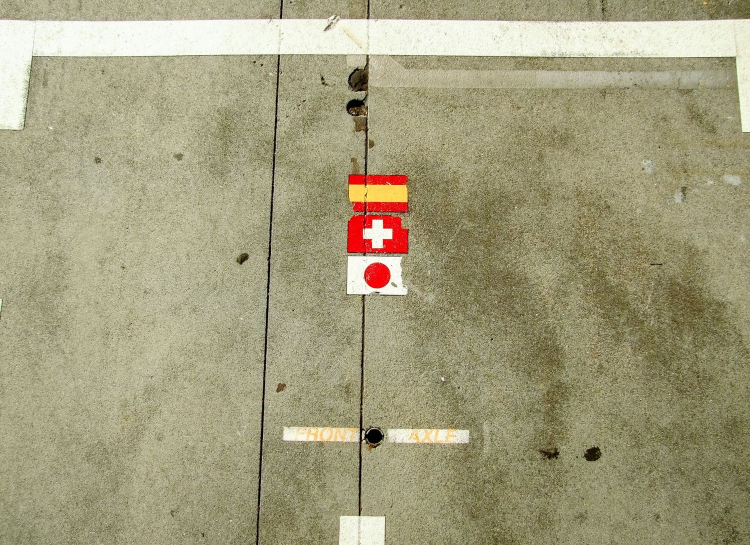 Trois petits autocollants représentant les drapeaux espagnol, suisse et japonais alignés sur le circuit F1 de Melbourne par Jérémie Botte.