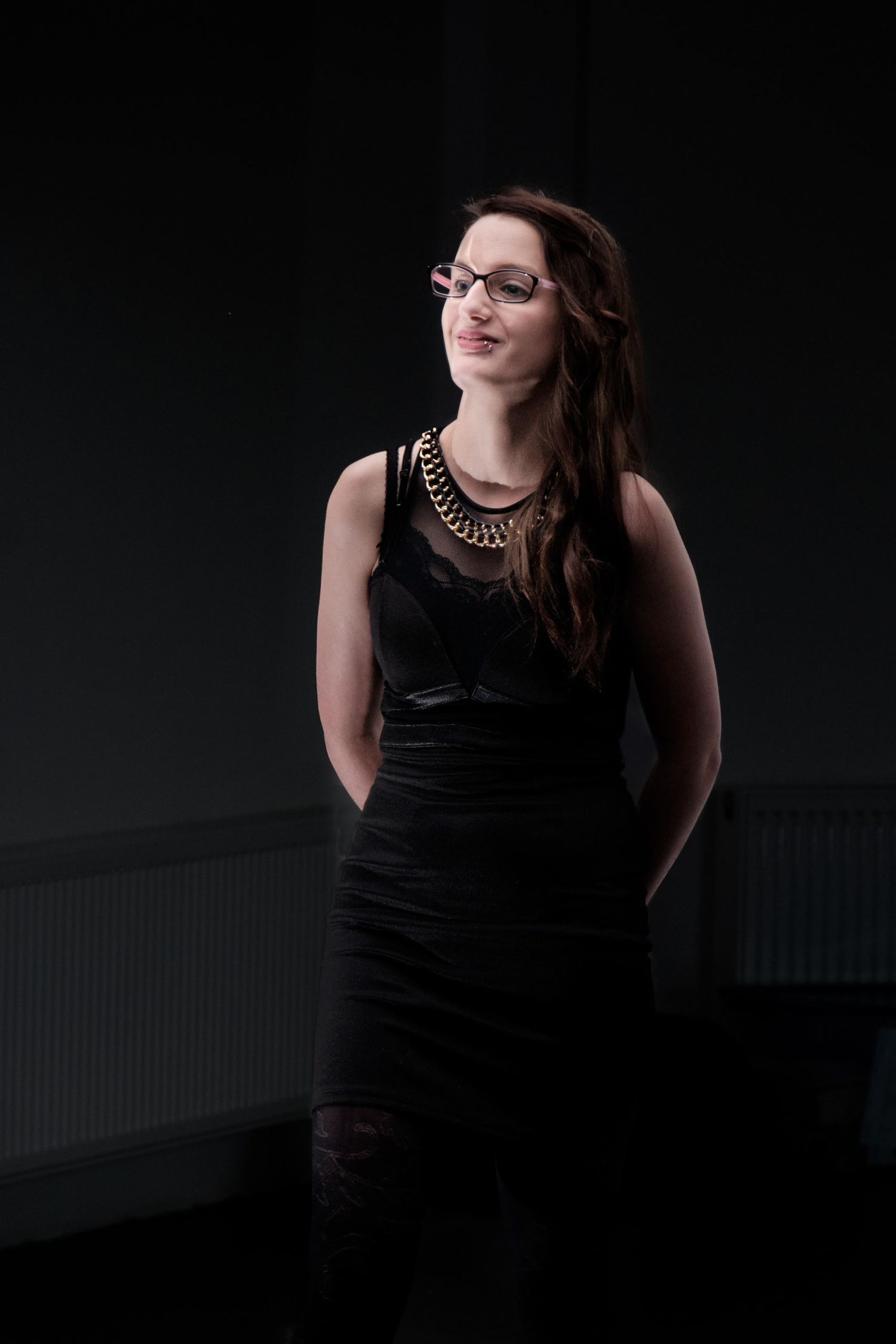 Portrait d'une jeune femme à lunettes en robe noire sur fond sombre, par Jérémie Botte.