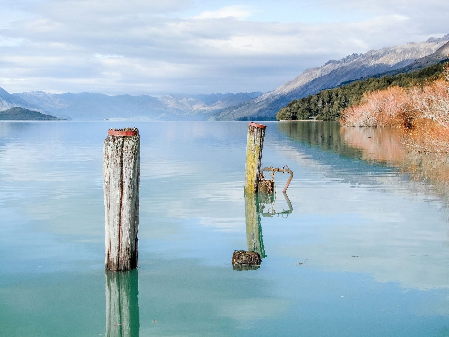 Photo de voyage en Nouvelle-Zélande montrant deux anciens poteaux en bois plantés dans une eau turquoise par Jérémie Botte.