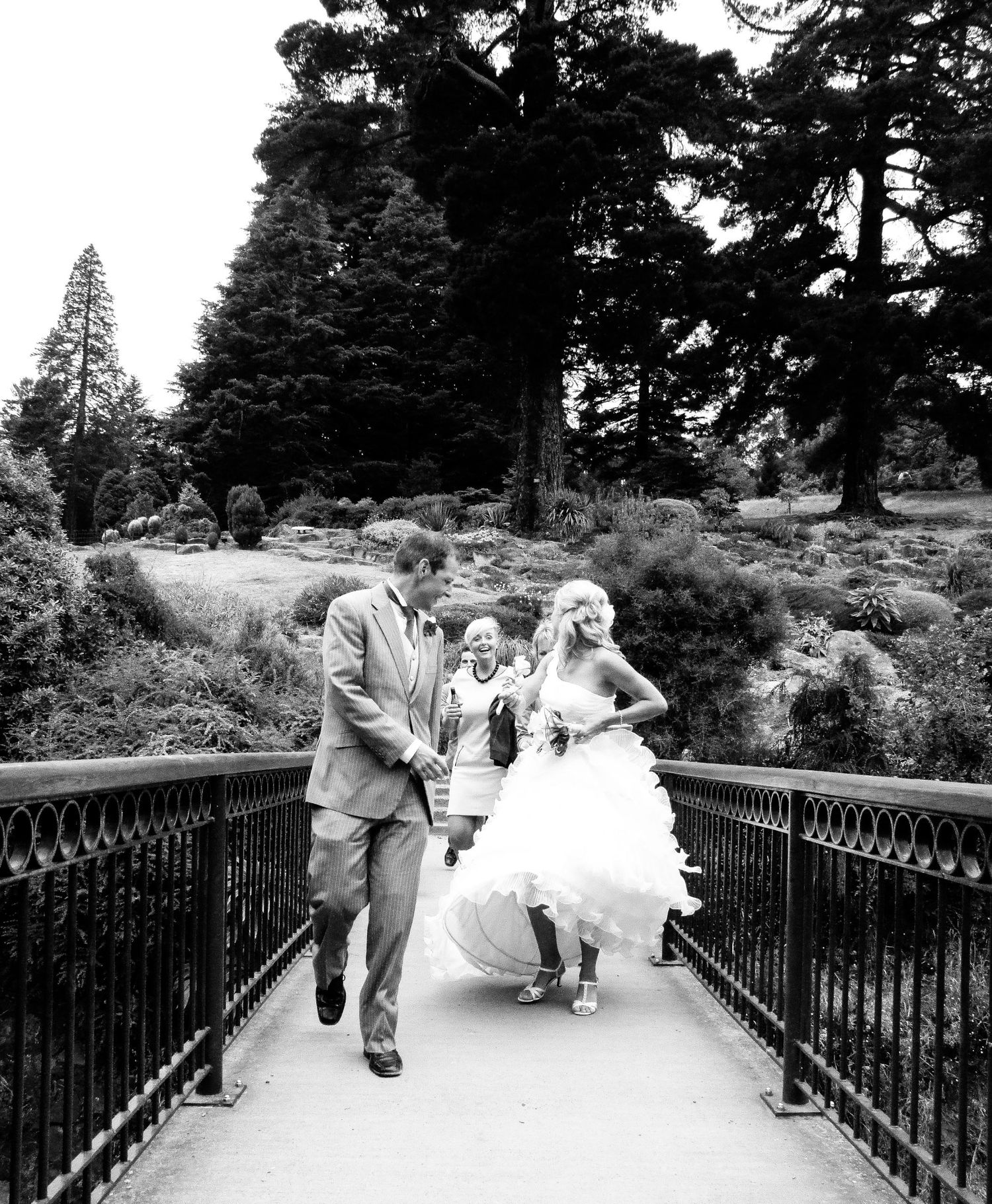 Les mariés en noir et blanc marchent et s'amusent spontanément sur une passerelle de jardin, par Jérémie Botte.