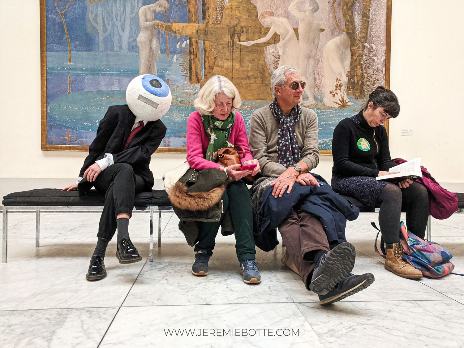 Une personne portant un masque en forme de globe oculaire géant est assise sur un banc du Musées royaux des Beaux-Arts de Bruxelles.