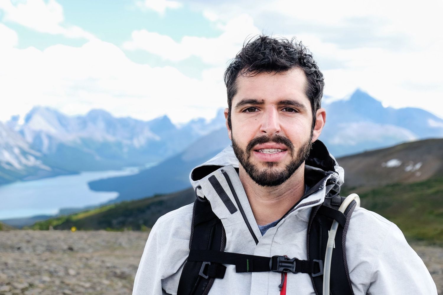 Portrait en gros plan d'un homme barbu en tenue de randonnée devant un lac de montagne pour le Portfolio de Jérémie Botte.