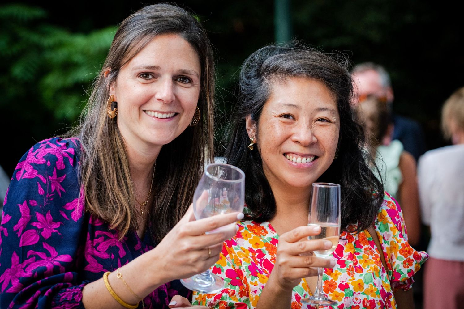Portrait de deux invitées souriantes qui trinquent face à l'objectif lors d'une réception de mariage en extérieur, par Jérémie Botte.