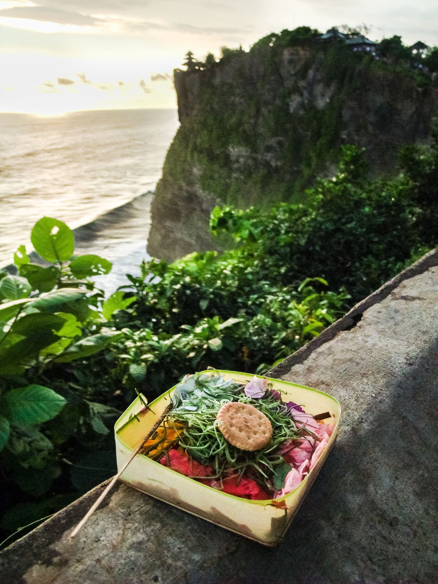 Une offrande traditionnelle posée sur un muret face à la falaise d'Uluwatu à Bali au coucher du soleil, par Jérémie Botte.