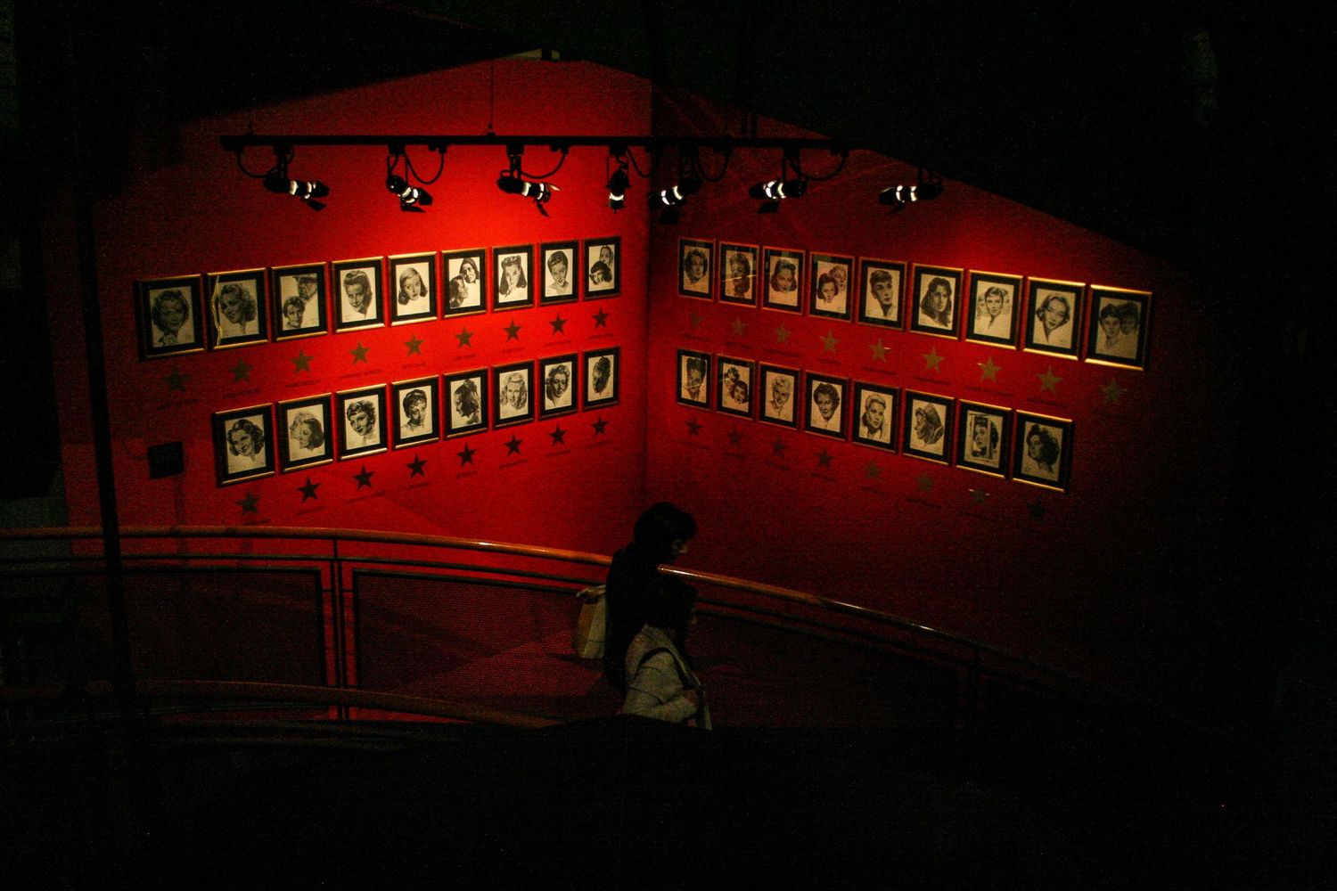 Une personne descend un escalier plongé dans le noir face à un mur rouge couvert de portraits encadrés au Mole Antonelli par Jérémie Botte.