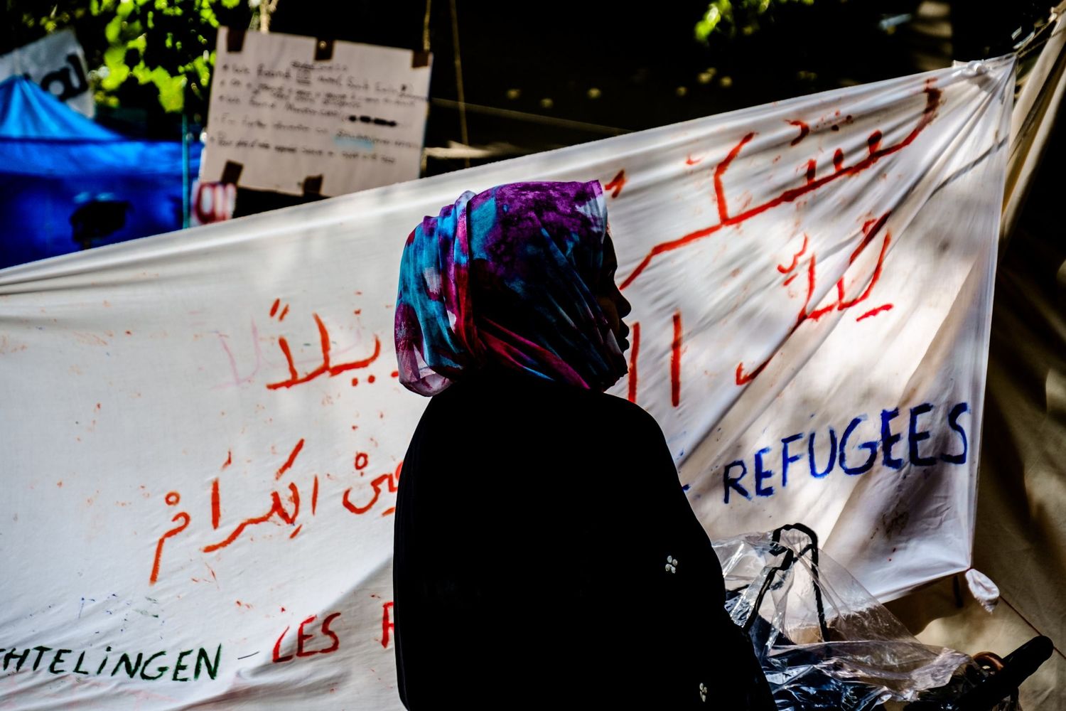 Silhouette en contre-jour d'une femme voilée devant une banderole de soutien aux réfugiés par Jérémie Botte.