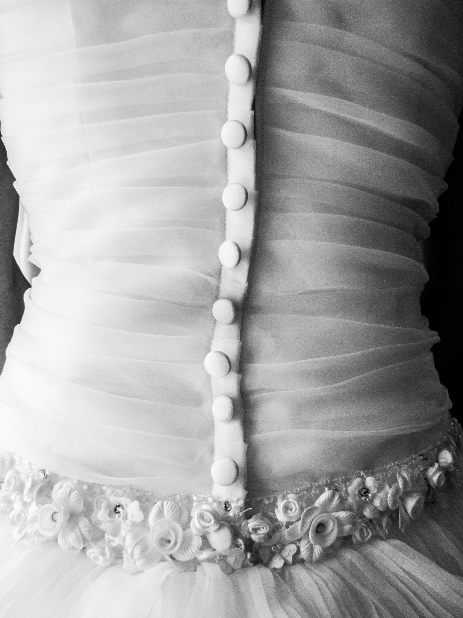 Plan détaillé du dos d'une robe de mariée, montrant la rangée de boutons et la ceinture ornée, photo noir et blanc par Jérémie Botte.