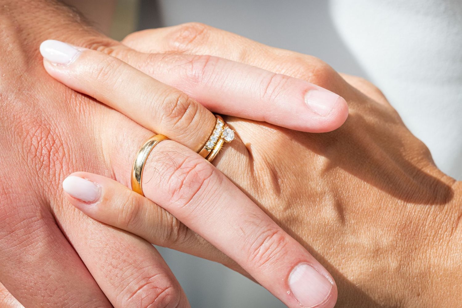 Gros plan sur les mains entrelacées d'un couple marié, mettant en valeur leurs alliances et une bague de fiançailles, par Jérémie Botte.