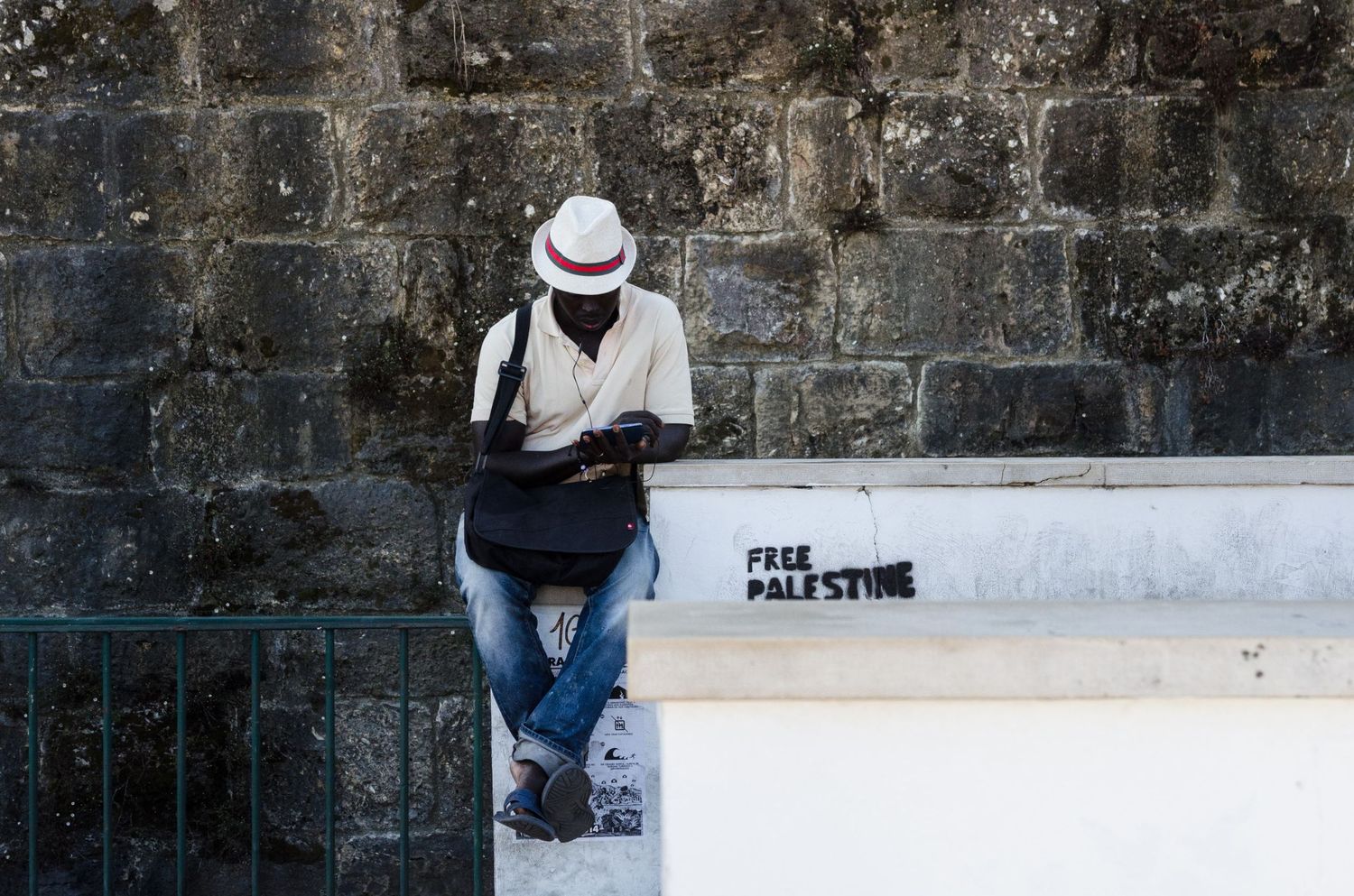 Un homme coiffé d'un chapeau blanc regarde son téléphone assis par Jérémie Botte.