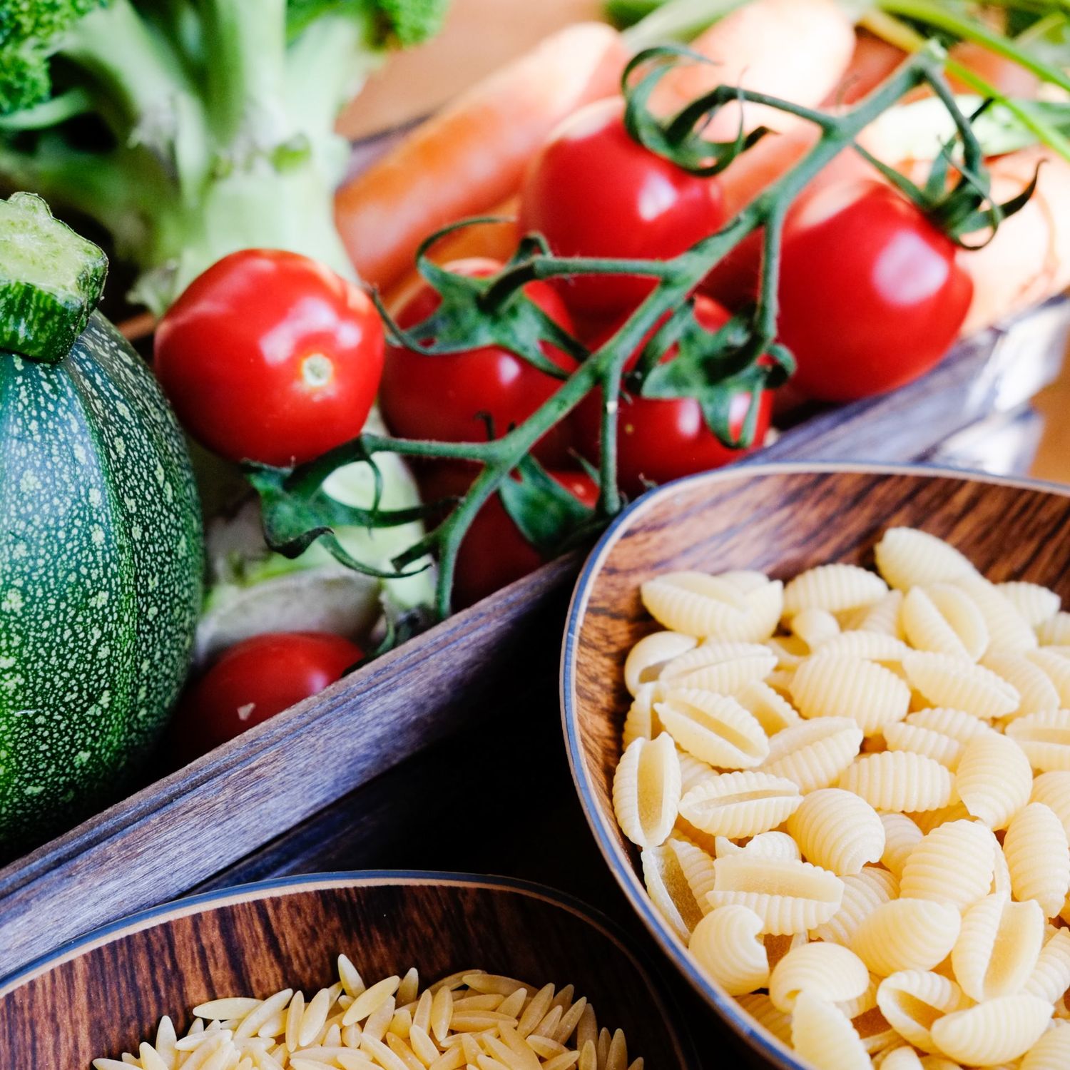 Gros plan sur des bols de pâtes fraîches et de céréales entourés de tomates cerises et d'une courgette par Jérémie Botte.