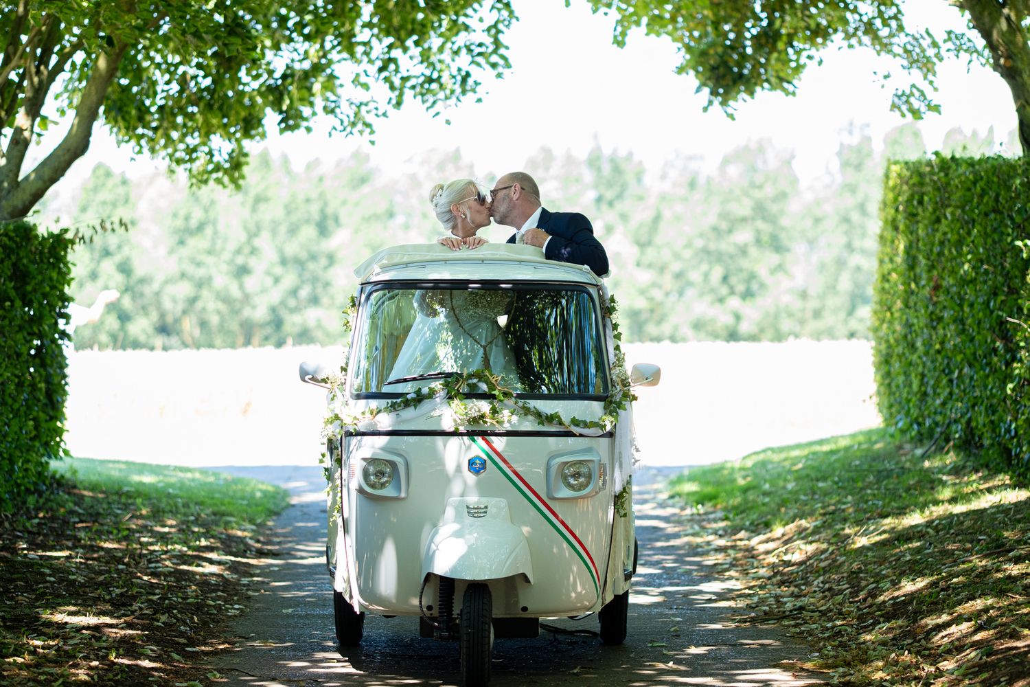 Photographie de mariage en exterieur de jour des deux mariés s'embrassant dans une voiturette italienne par le photographe Jérémie Botte.
