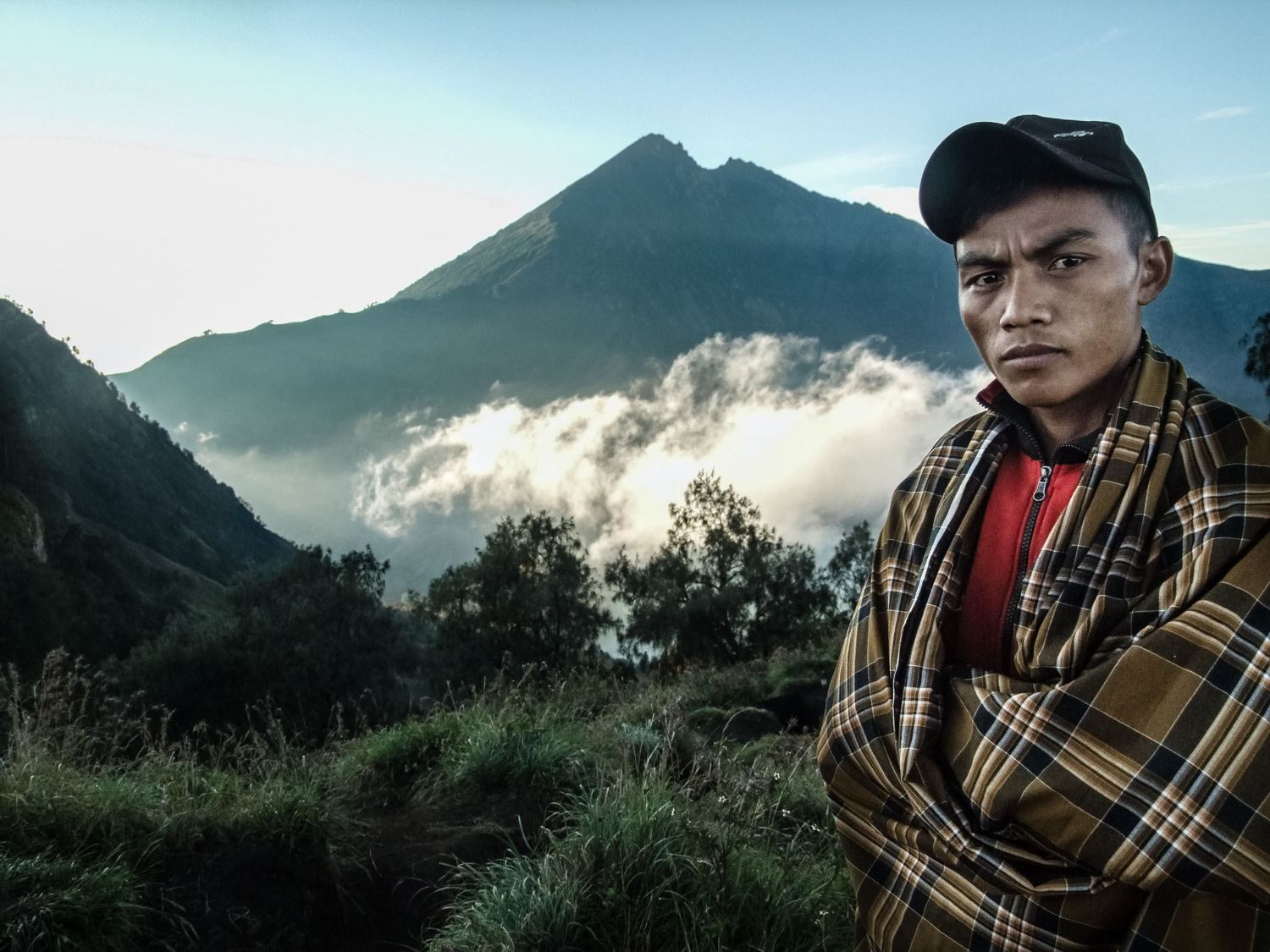 Portrait de voyage en Indonésie d'un homme en habit traditionnel avec le volcan Rinjani en arrière-plan par le photographe Jérémie Botte.