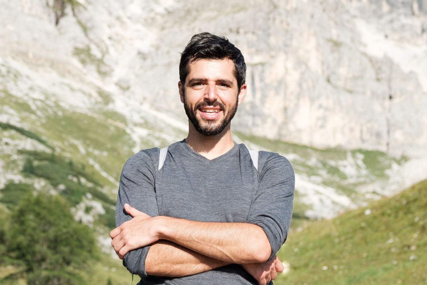 Portrait d'un homme souriant, les bras croisés, devant une montagne rocheuse ensoleillée pour le Portfolio de Jérémie Botte.