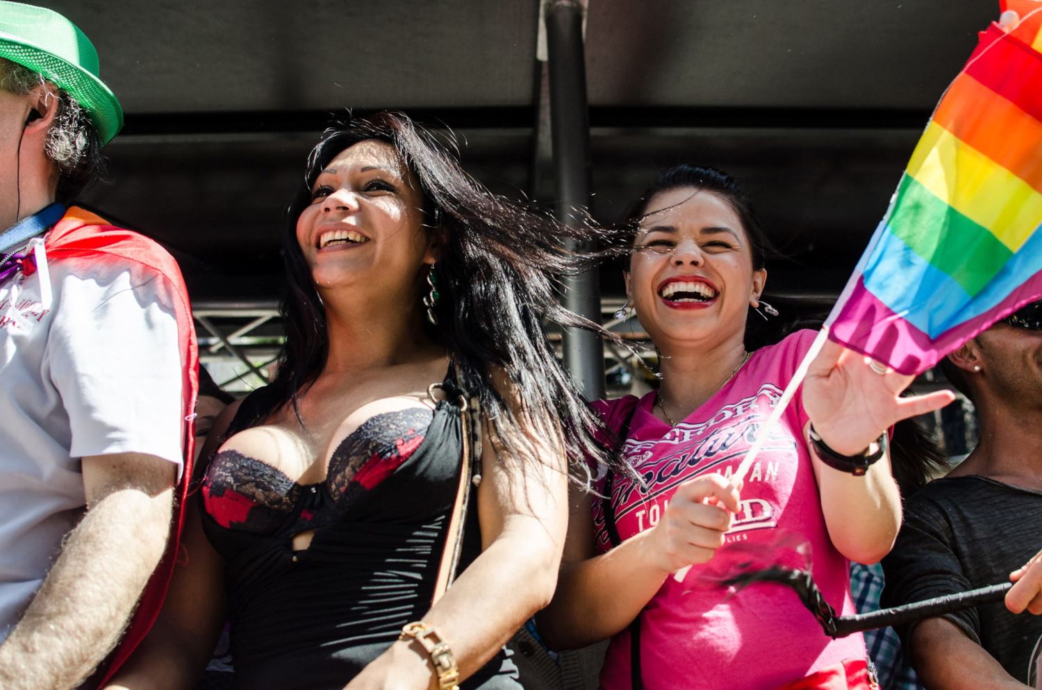Deux femmes sourient joyeusement au milieu d'une foule en agitant un drapeau arc-en-ciel de la Gay Pride par Jérémie Botte.