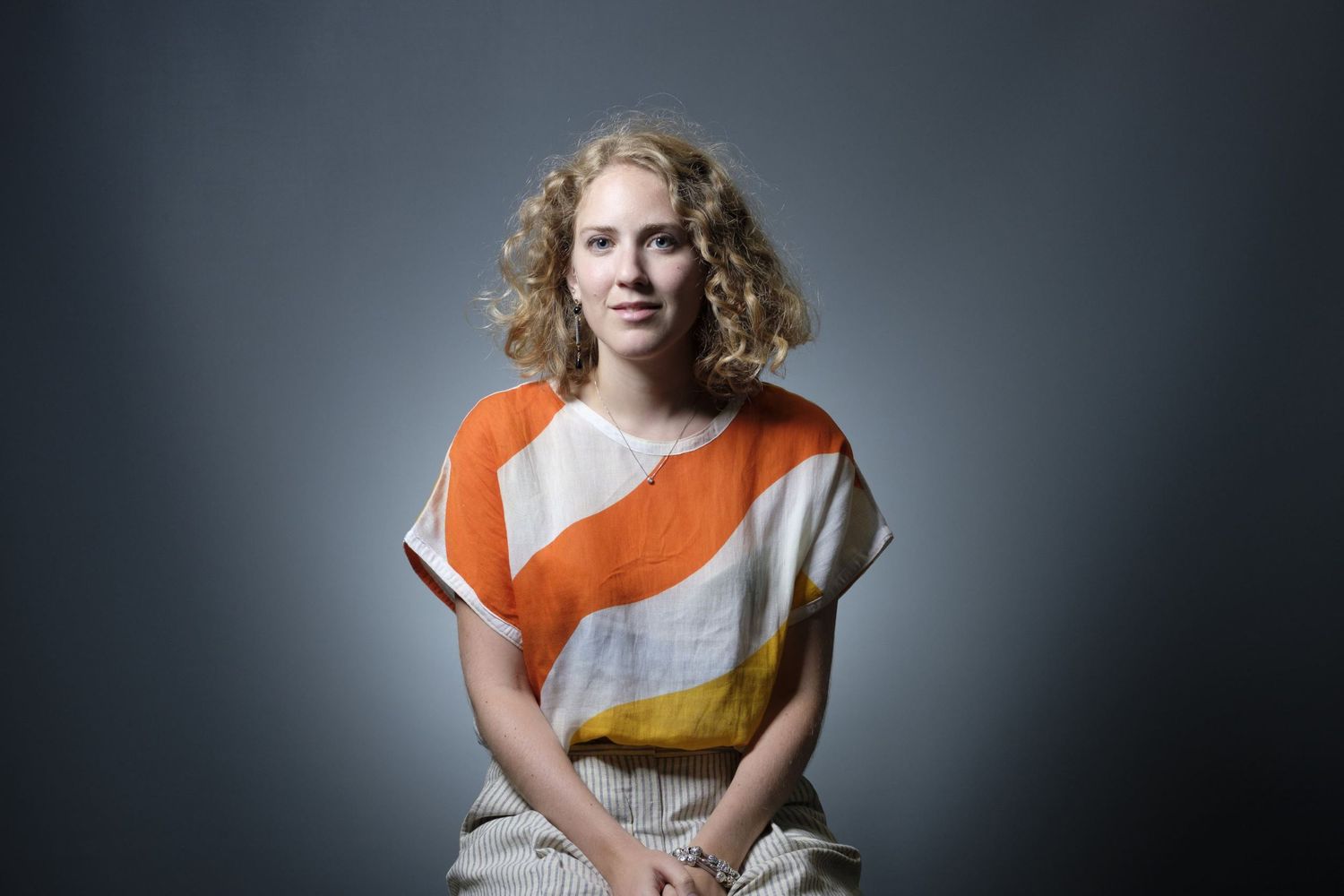 Portrait professionnel en studio d'une femme aux cheveux bouclés portant un haut rayé orange et blanc par le photographe Jérémie Botte.