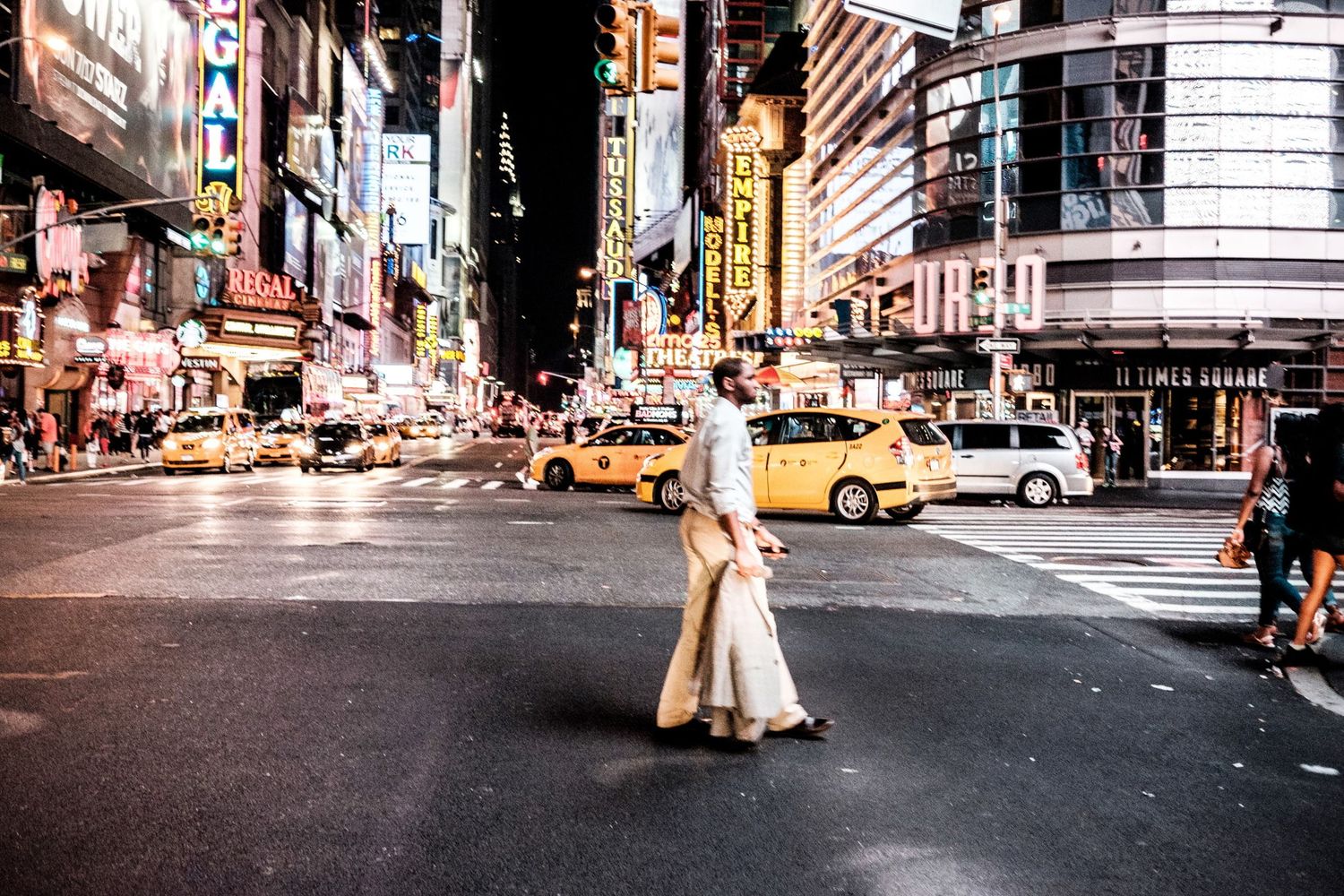 Un homme traverse un carrefour de Times Square à New York au milieu des taxis jaunes de nuit par Jérémie Botte.
