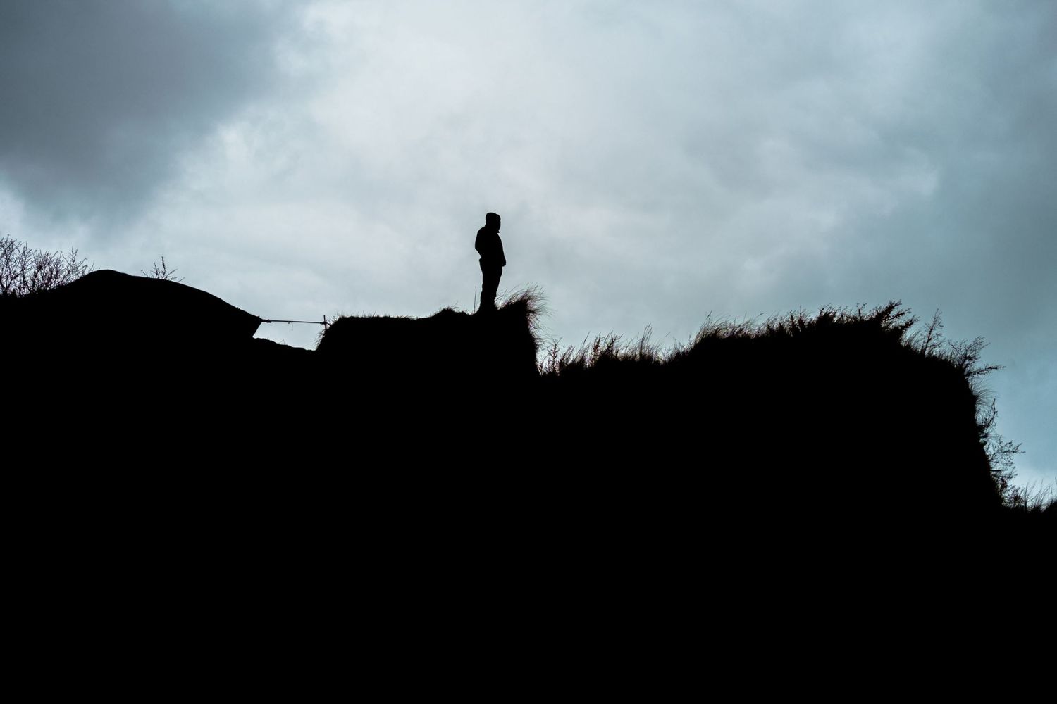 Silhouette sombre d'une personne seule debout au sommet d'une falaise sous un ciel très nuageux par Jérémie Botte.