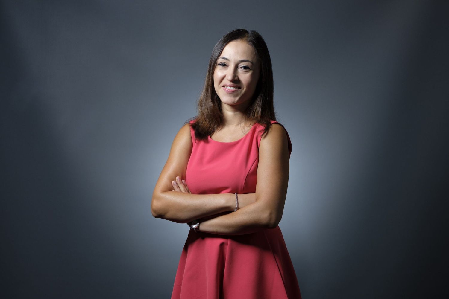 Portrait en studio d'une femme souriante en robe rose les bras croisés par le photographe de portrait Jérémie Botte à Bruxelles.