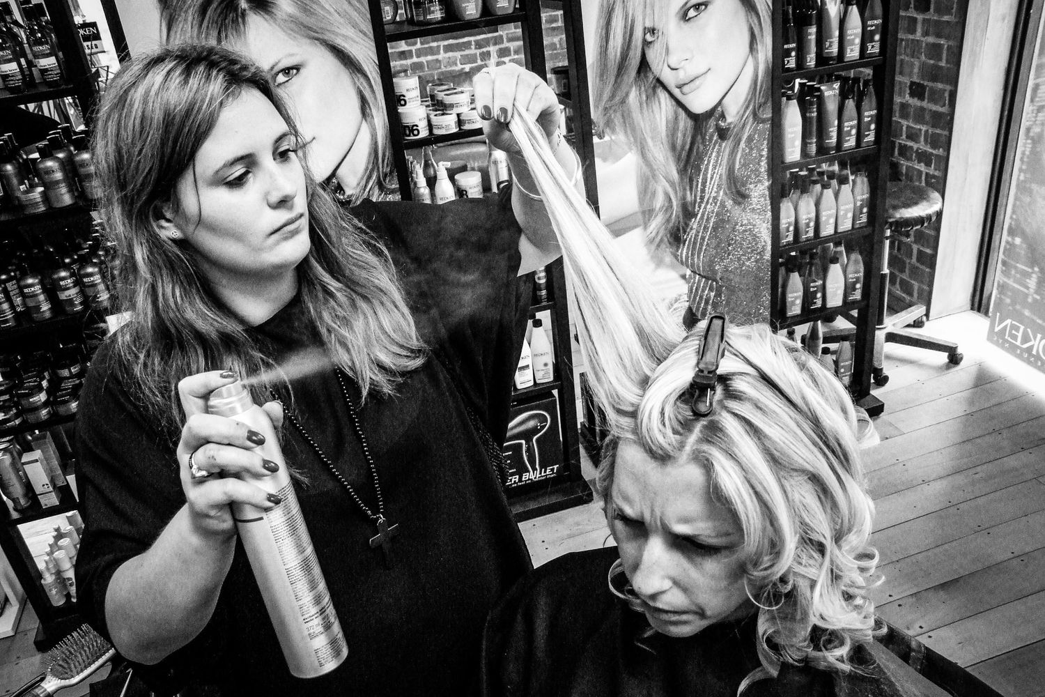 Préparation de la mariée au salon de coiffure, coiffeuse vaporisant de la laque sur une mèche, photo noir et blanc par Jérémie Botte.