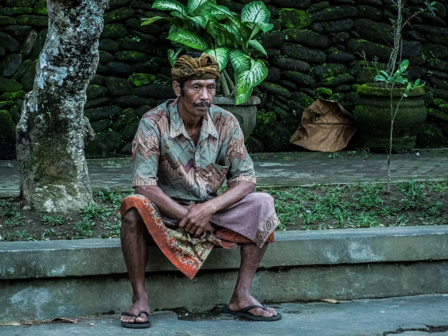 Un homme en tenue traditionnelle assis sur un muret en Indonésie, par Jérémie Botte.
