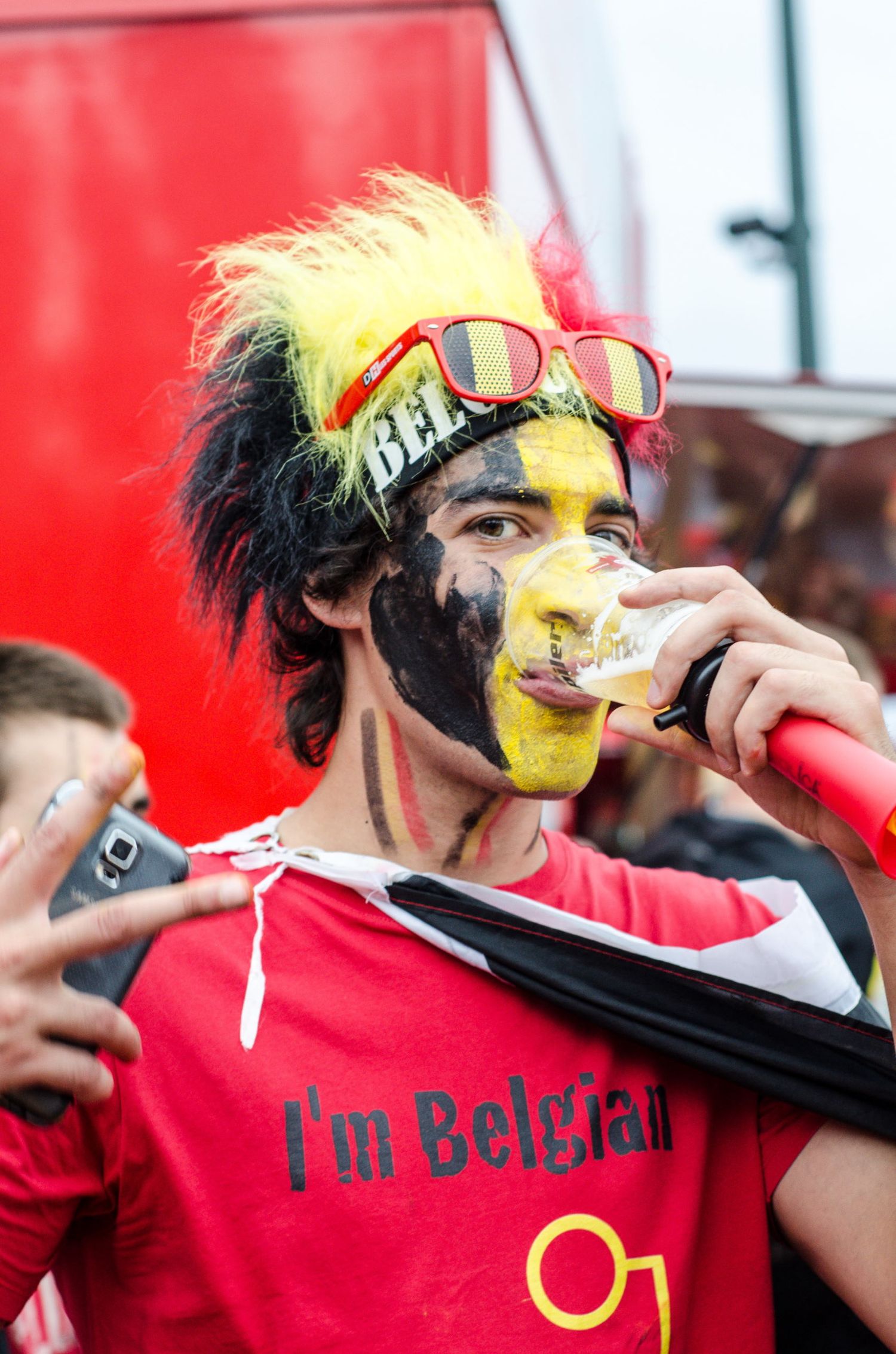 Portrait d'un supporter belge grimé aux couleurs de son pays, buvant une bière dans la foule par Jérémie Botte.