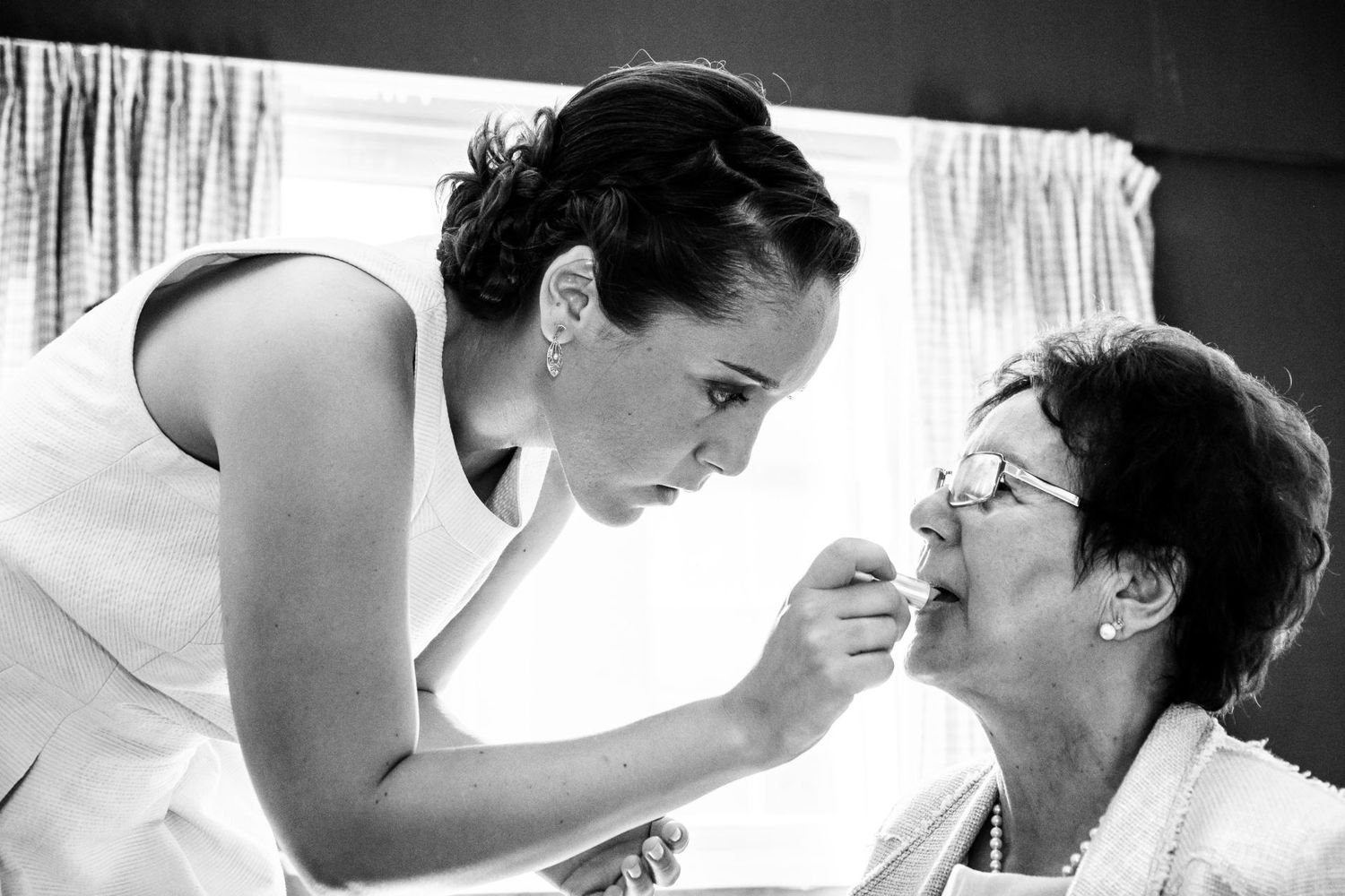 Une future mariée appliquant délicatement du rouge à lèvres sur sa maman portant des lunettes, par Jérémie Botte.