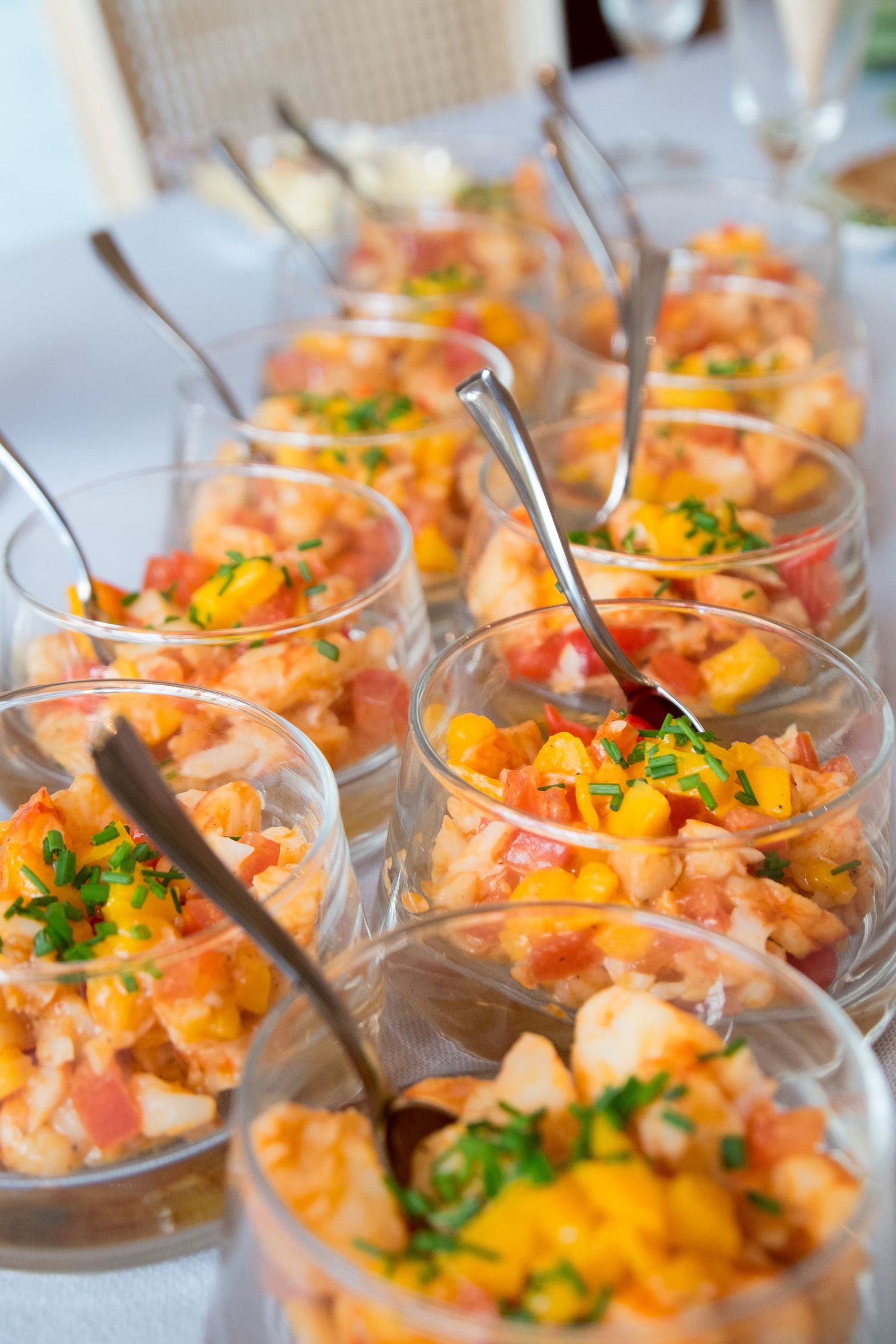 Plusieurs petits verres alignés contenant un tartare ou une verrine colorée aux dés de mangue, agrémentés de ciboulette ciselé, par J Botte.