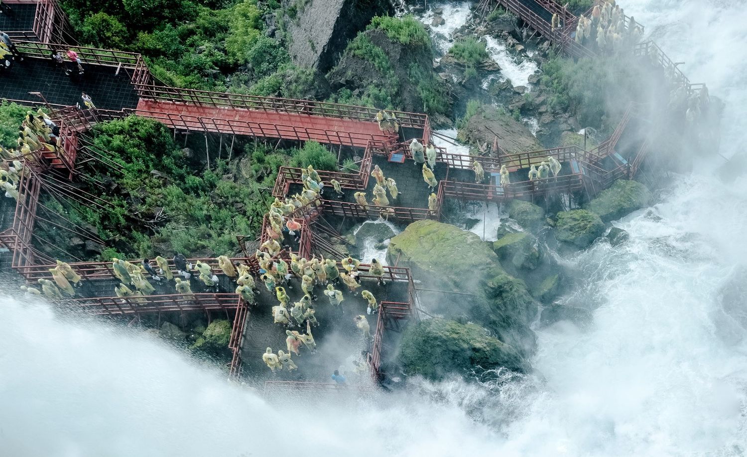 Vue plongeante sur des touristes en imperméables jaunes visitant des passerelles au pied des chutes du Niagara par Jérémie Botte.